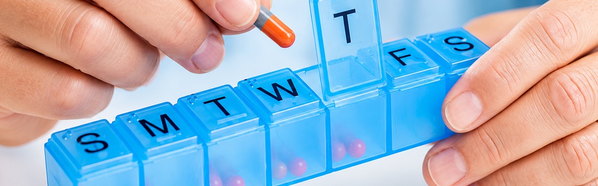 A patient loading a weekly pill organiser, one dose per day of the week